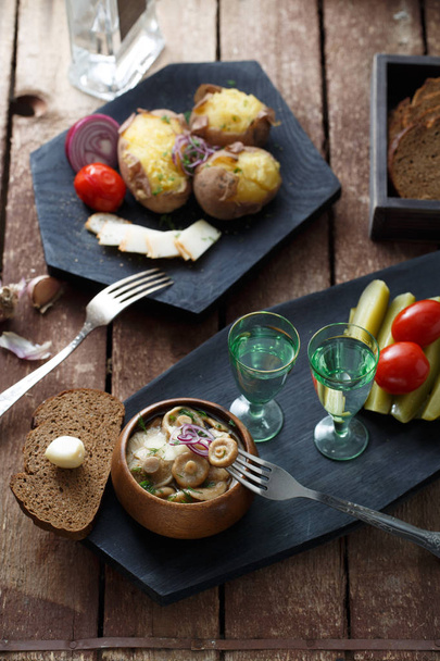 Nakládaná rajčata, okurky, žampiony a cibulí na dřevěné pozadí s vidličkou a skleničkami vodky. - Fotografie, Obrázek