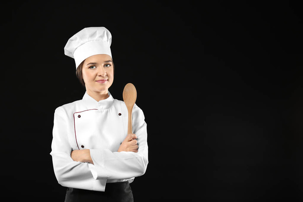 Portrait of female chef with wooden spoon on black background - Фото, изображение