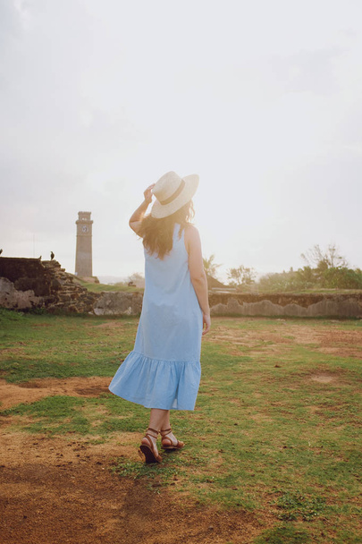 Young woman in a hat walks in the fortress walls at sunset - Foto, afbeelding