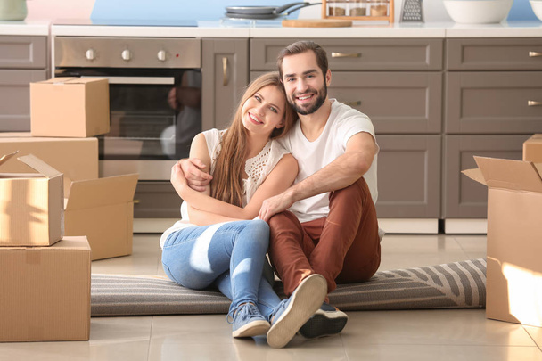 Young couple with moving boxes on floor in kitchen at new home - Фото, изображение