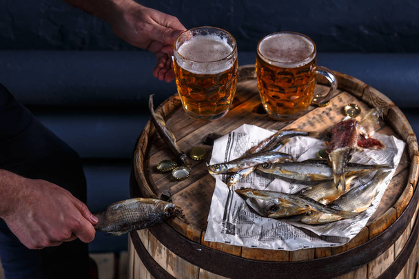 Beer mugs with dried fishes on a wooden barrel - Foto, Bild