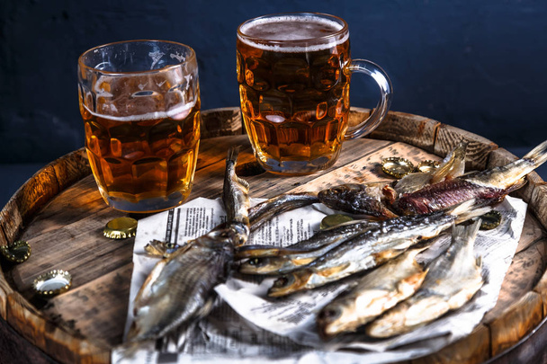 Bierkrüge mit getrockneten Fischen auf einem Holzfass - Foto, Bild
