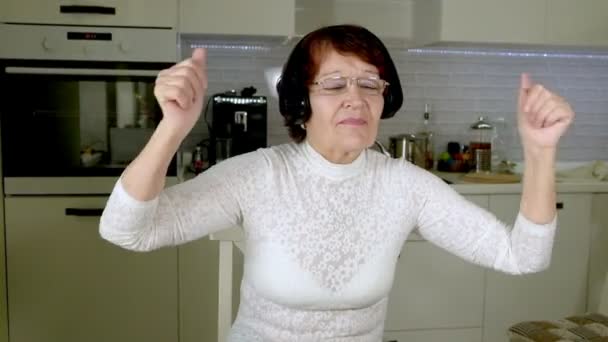 Yaşlı bir kadın telefondan kulaklıklar müzik dinler, enerjik gesticulates ve dans ediyor - Video, Çekim
