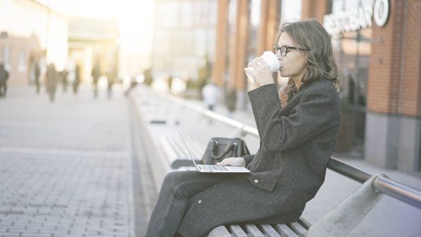 Young businesswoman with a laptop drinking coffee, street - Φωτογραφία, εικόνα