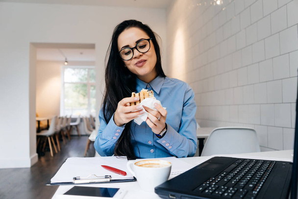 happy woman sitting in the office and eating a sandwich - 写真・画像