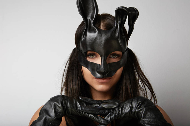 Sexy woman wearing a black mask Easter bunny standing on a white background and looks very sensually. - Photo, Image