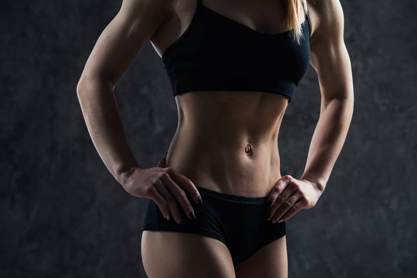 Sportowe sexy dziewczyna z big mięśni brzucha w czarny odzież sportowa na czarnym tle. Sześciopak na brzuchu w kolorze czarnym. Taut, pompowane, firma brzuch - Zdjęcie, obraz