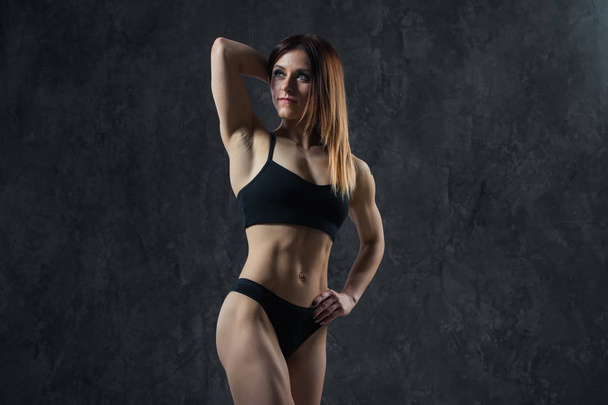 Sports sexy girl with big muscle belly in a black sportswear on a black background. A six-pack on his stomach in black color. Taut, pumped up, firm abdomen - Photo, Image