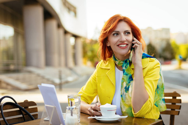 Smiling businesswoman using phone on a coffee break in a street cafe. - Foto, afbeelding