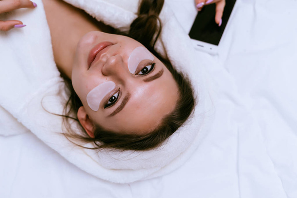 cute young girl lies on a bed in a white coat, under the eyes white patches - Foto, afbeelding