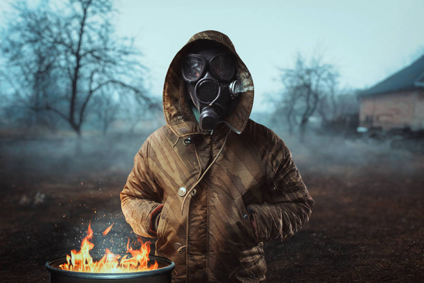stalker soldier in gas mask near fireplace, survivor man after nuclear war. Post apocalyptic lifestyle - Photo, Image