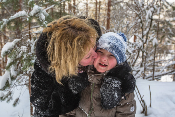 Jonge vrouw speelt met een zijn zoontje in een besneeuwde winter Park. - Foto, afbeelding