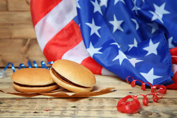Tasty hamburgers on wooden table against blurred American flag - Fotó, kép