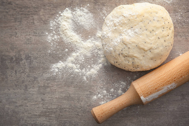 Raw dough with poppy seeds and rolling pin on table - Foto, afbeelding