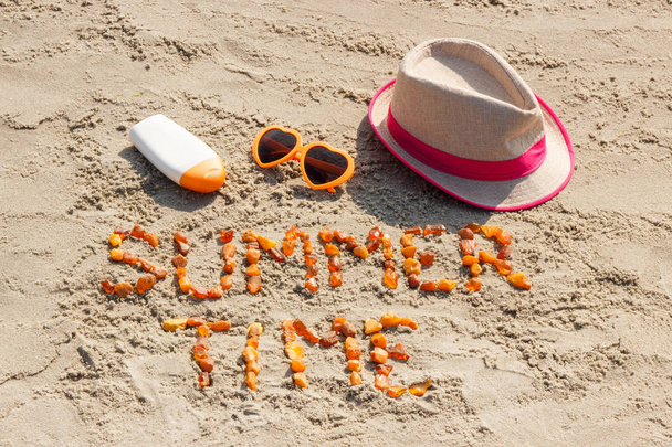 Inscription heure d'été, lunettes de soleil, crème solaire et chapeau de paille sur le sable à la plage
 - Photo, image