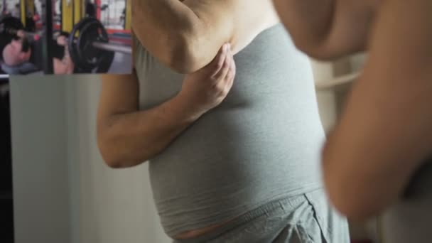 Pulchny człowiek ogląda lekkoatletka mięśni na zdjęcie i dotykając jego tłuszczu z brzucha - Materiał filmowy, wideo
