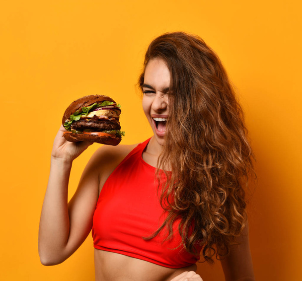 Woman eat burger sandwich with hungry mouth on yellow background - Photo, Image