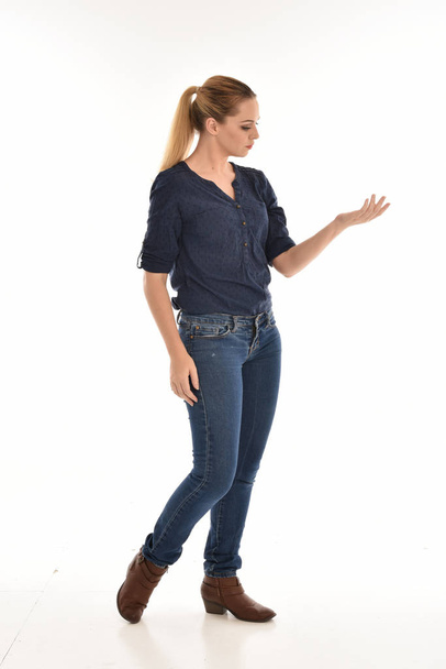 volledige lengte portret van het meisje dragen van eenvoudige blauw shirt en spijkerbroek, permanent pose.isolated op witte studio achtergrond. - Foto, afbeelding