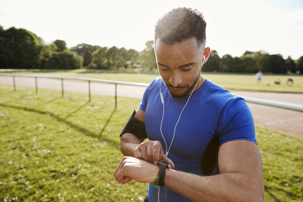 Hombre joven en pista de atletismo ajuste aplicación en smartwatch
 - Foto, Imagen