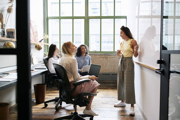 Woman standing at whiteboard in a meeting with female team - Foto, Imagen