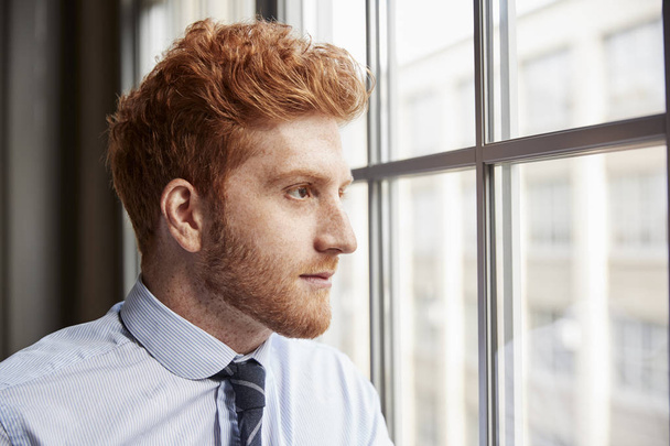 Young red haired bearded businessman looking out of window - Φωτογραφία, εικόνα
