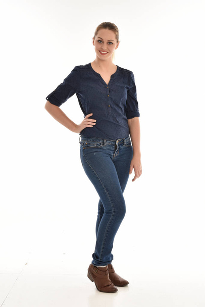 Ganzkörperporträt eines Mädchens, das einfaches blaues Hemd und Jeans trägt, in posierender Haltung auf weißem Studiohintergrund. - Foto, Bild