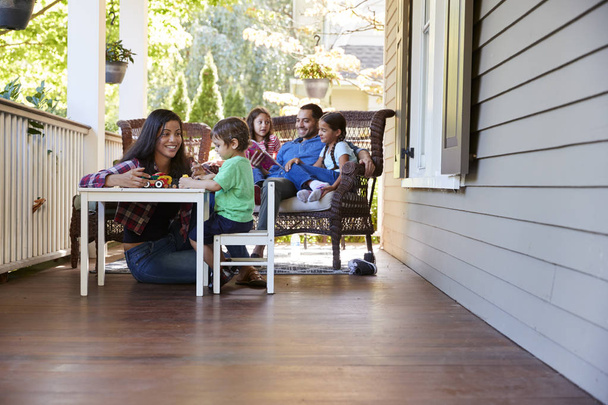 Family Sit On Porch Of House Reading Books And Playing Games - Photo, Image