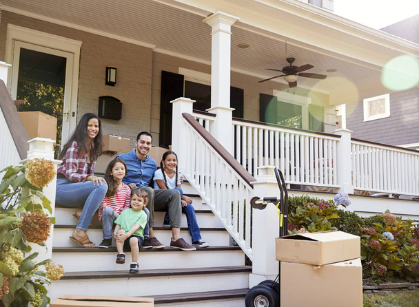 Family Sitting On Steps Of New Home On Moving In Day - Photo, image