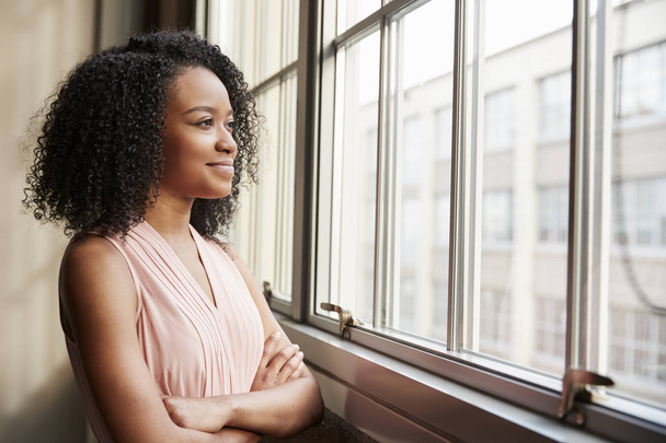 Young black woman with arms crossed looking out of window - Foto, Imagem
