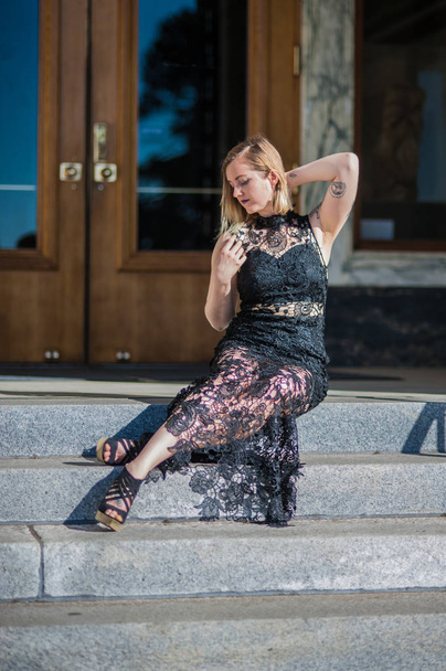 Young woman reclined across entrance steps in sexy black lace evening gown. - Photo, Image