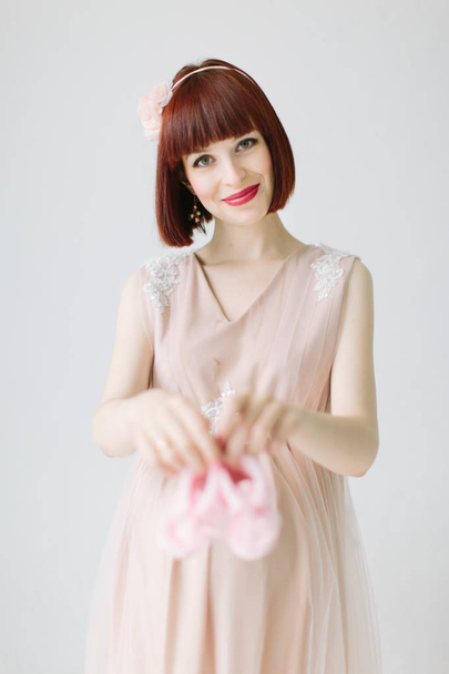 portrait of happy pregnant woman in pink dress holding pink shoes for baby - Fotoğraf, Görsel