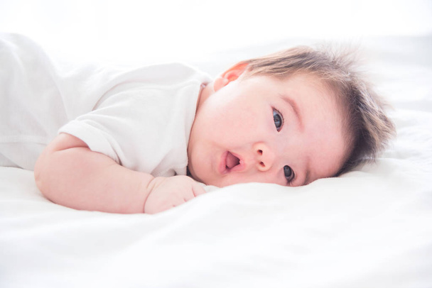 Säugling wacht morgens auf weißem Bett auf - Foto, Bild