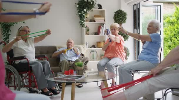 Enfermera joven mostrando grupo de ancianos algunos ejercicios con una banda de resistencia en el hogar de ancianos
. - Metraje, vídeo