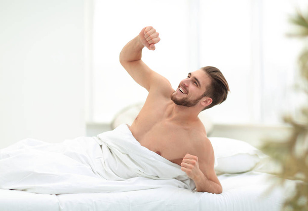 lächelnder Mann wacht in einem gemütlichen Schlafzimmer auf - Foto, Bild