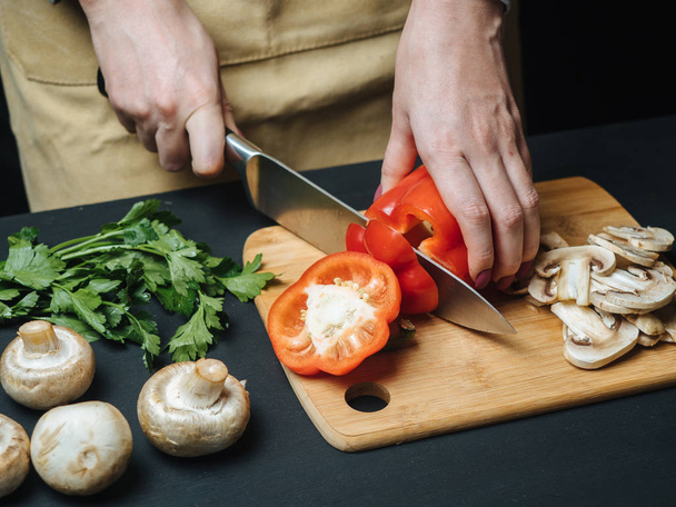 Woman cutting raw red pepper on wooden board - Photo, image