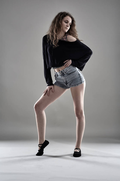 Young female dancer wearing shorts and blouse standing against gray background - Фото, зображення