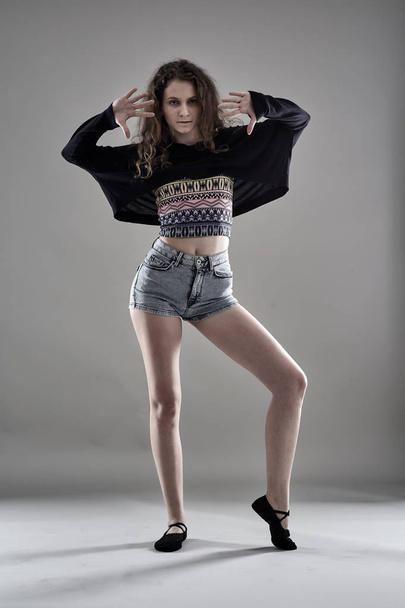 Young female dancer wearing shorts and blouse standing against gray background - Foto, immagini
