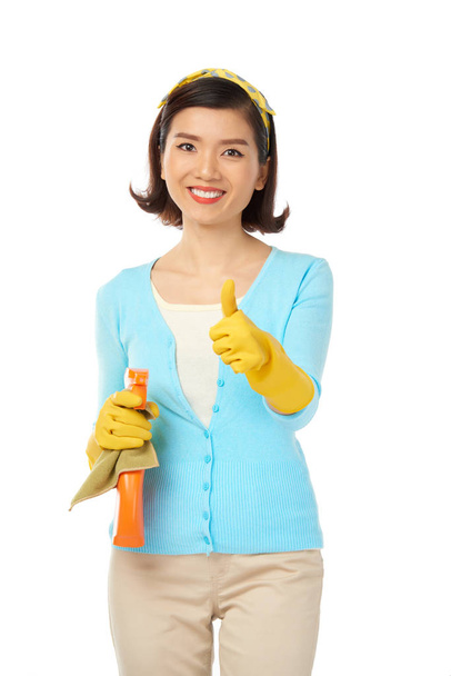 Mooie jonge huisvrouw dragen van rubberen handschoenen en duim opdagen - Foto, afbeelding