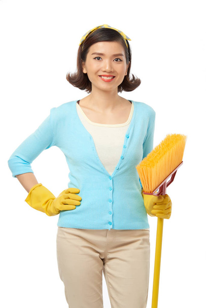 attraktive junge Haushälterin trägt Gummihandschuhe mit Besen in den Händen und posiert - Foto, Bild