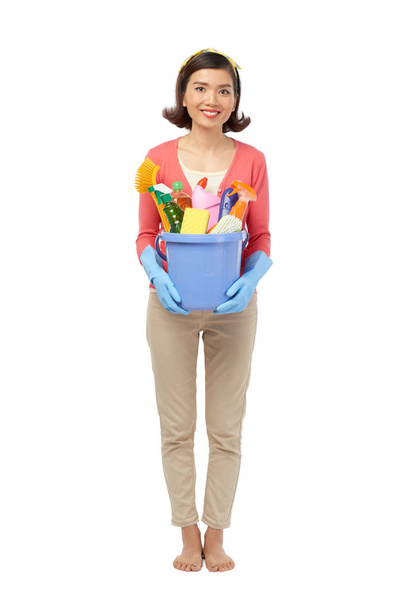 Full length portrait of cheerful young woman standing against white background and posing for photography with cleaning utensils in hands - Foto, Imagem