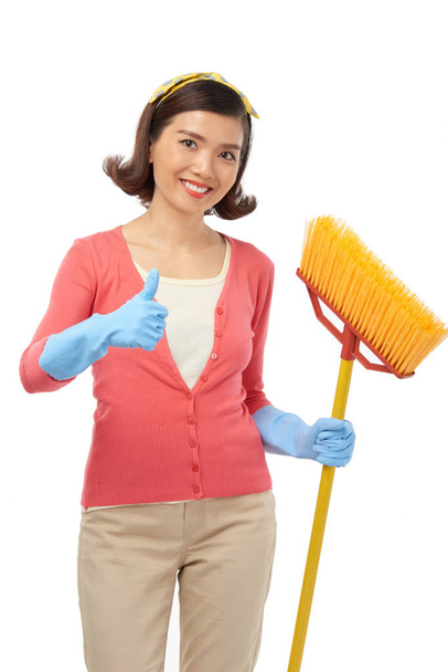 Confident young housekeeper with toothy smile showing thumb up to camera, isolated on white background - Zdjęcie, obraz
