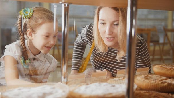 Chica con una coleta y su mamá miran los pasteles en la ventana eligiendo
 - Foto, imagen