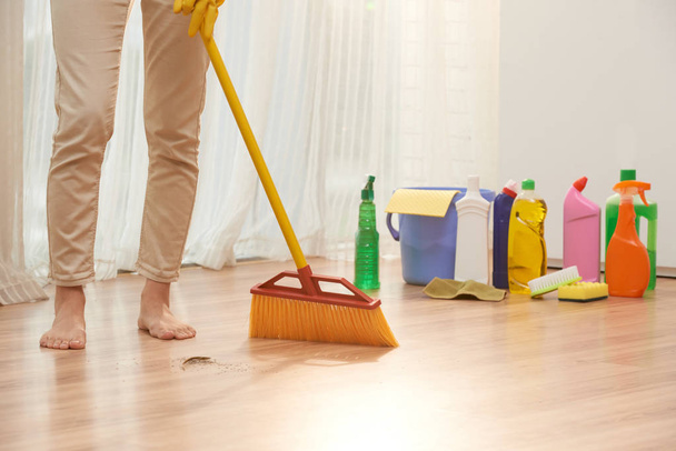 ξυπόλυτος γυναίκα σκουπίζοντας το πάτωμα με σκούπα ενώ τυλιγμένη σε βεράντες - Φωτογραφία, εικόνα