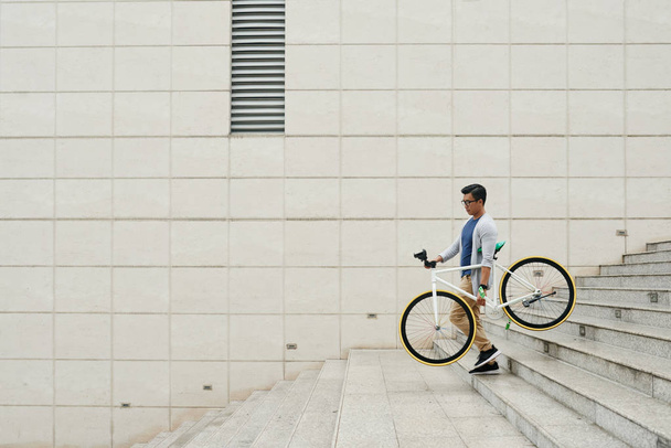 asiatischer Mann trägt Fahrrad und geht Treppe hinunter - Foto, Bild
