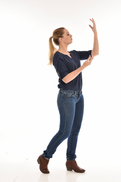 retrato de longitud completa de la niña con camisa azul simple y jeans, de pie en el perfil contra un fondo de estudio blanco
. - Foto, imagen