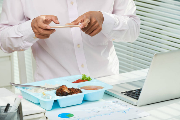Lähikuva kuva tunnistamaton johtaja yllään valkoinen paita seisoo toimistopöytä ja ottaa kuvan hänen lounas
 - Valokuva, kuva