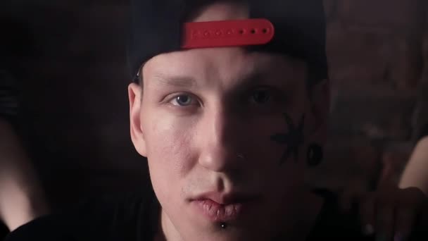Młode fajne człowieka w snapback z tatuażami twarz przed murem z dziewczynami - Materiał filmowy, wideo