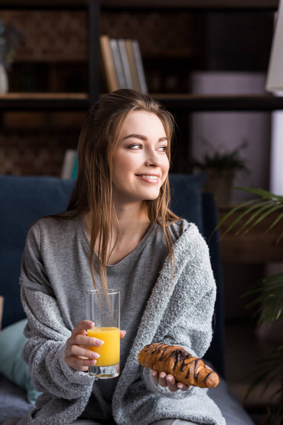 smiling girl holding glass of orange juice and croissant in morning - Fotografie, Obrázek