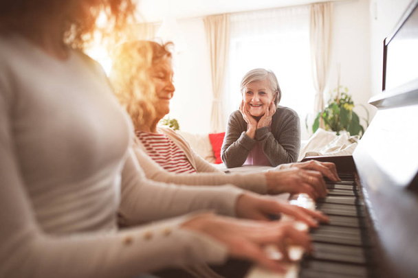 A girl with mother and grandmother playing the piano. - Foto, Bild