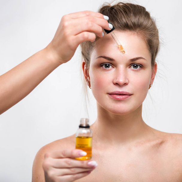 Portrait of a beautiful young woman with facial oil in hands - Photo, Image